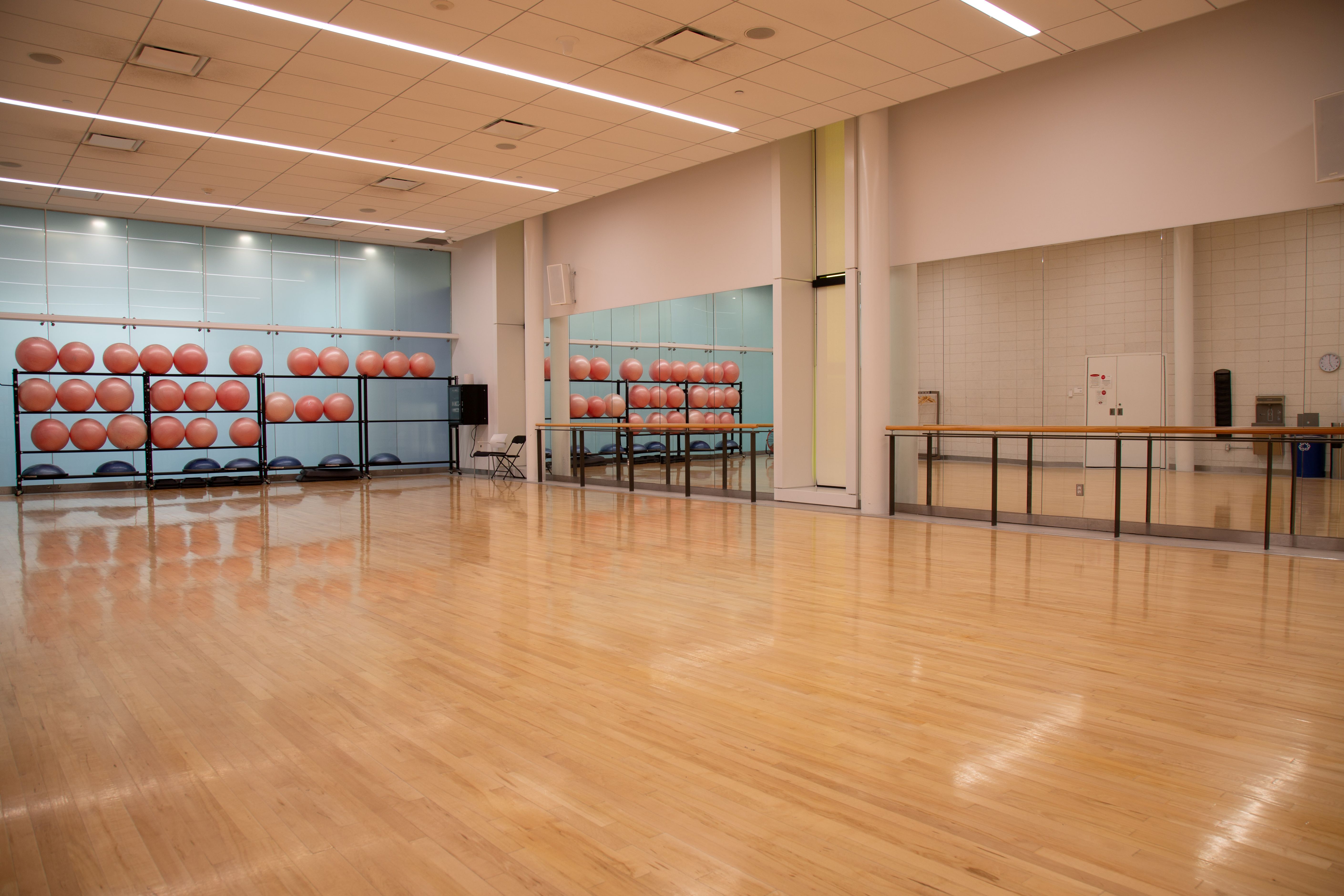 Spacious exercise room with polished wooden floor, mirrored wall, and racks holding multiple orange stability balls.