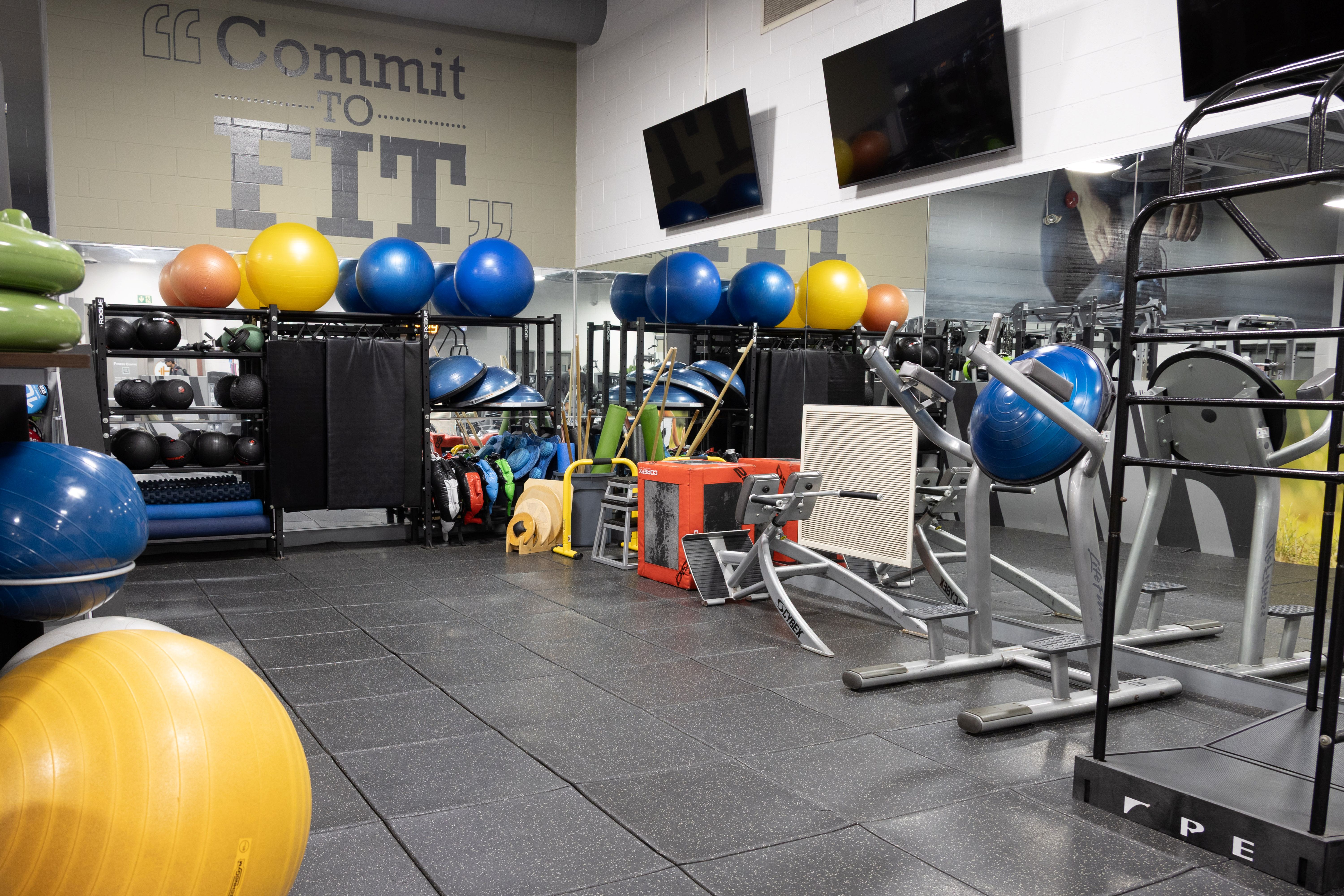 Indoor gym area with various exercise balls, weight racks, and fitness equipment against mirrored walls and motivational wall text.