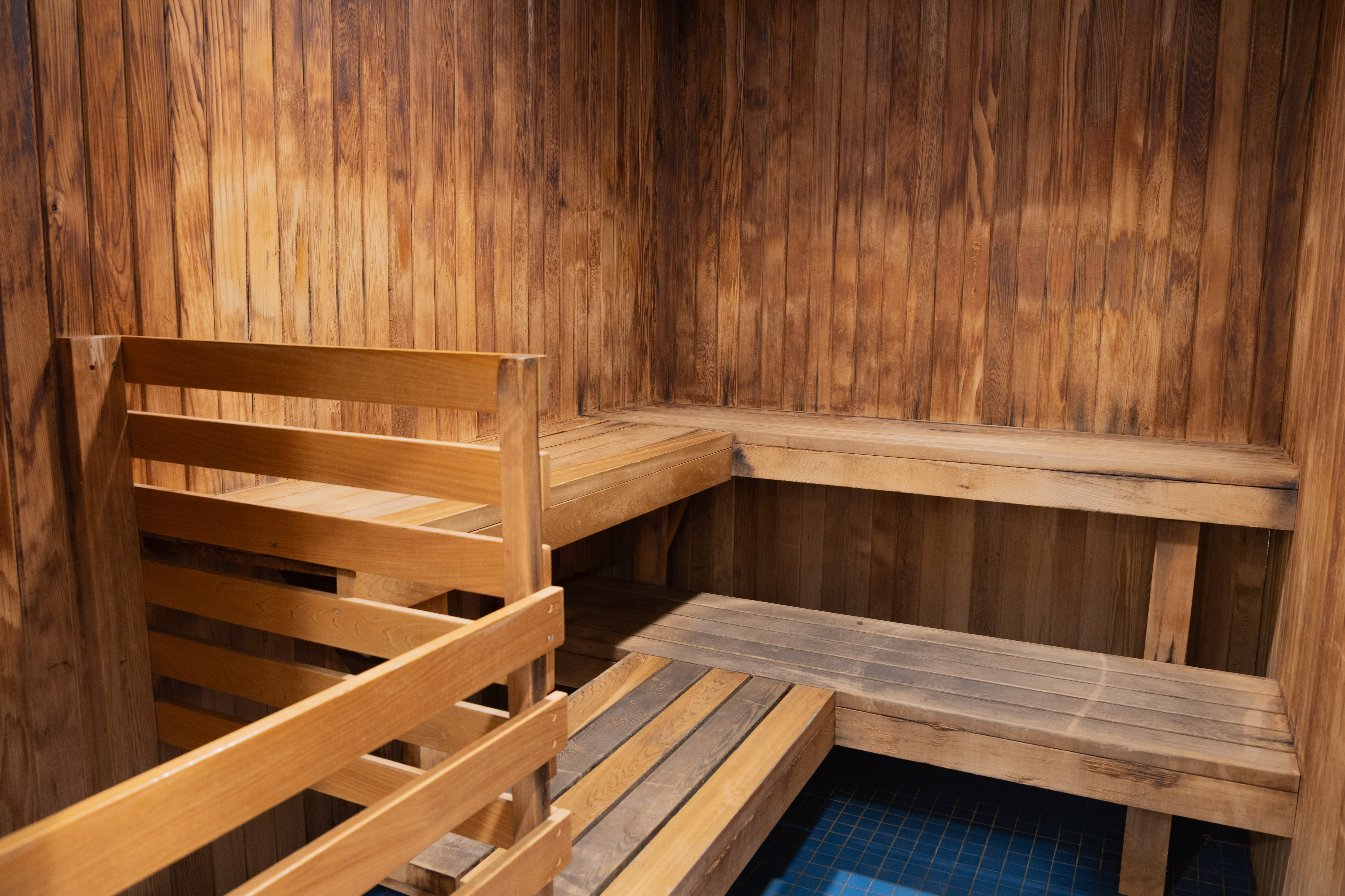 Interior of a wooden sauna room with tiered bench seating and warm lighting on the wood-paneled walls.