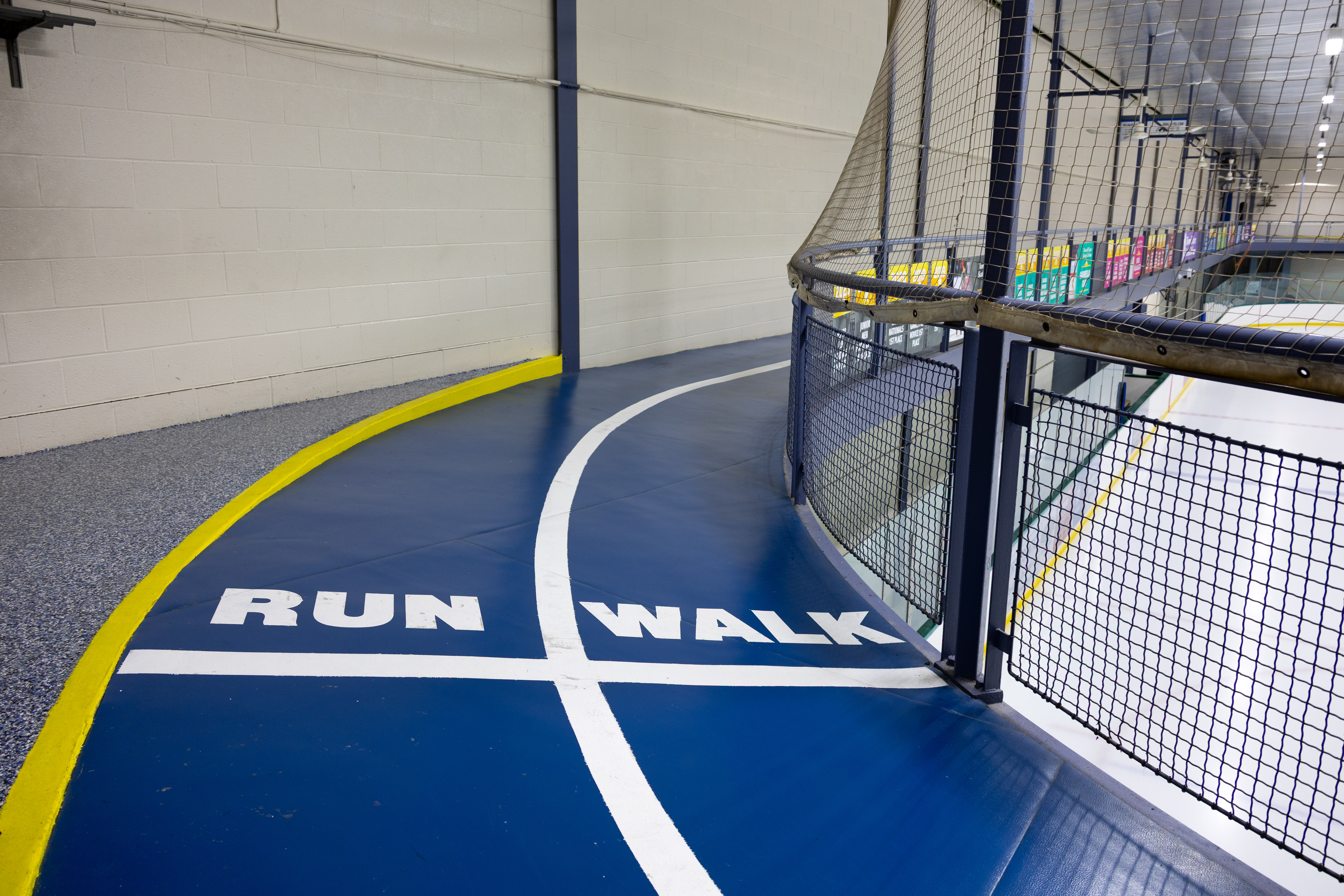 Indoor track with separate lanes marked 'RUN' and 'WALK' on a blue surface bordered by a yellow line and safety netting.