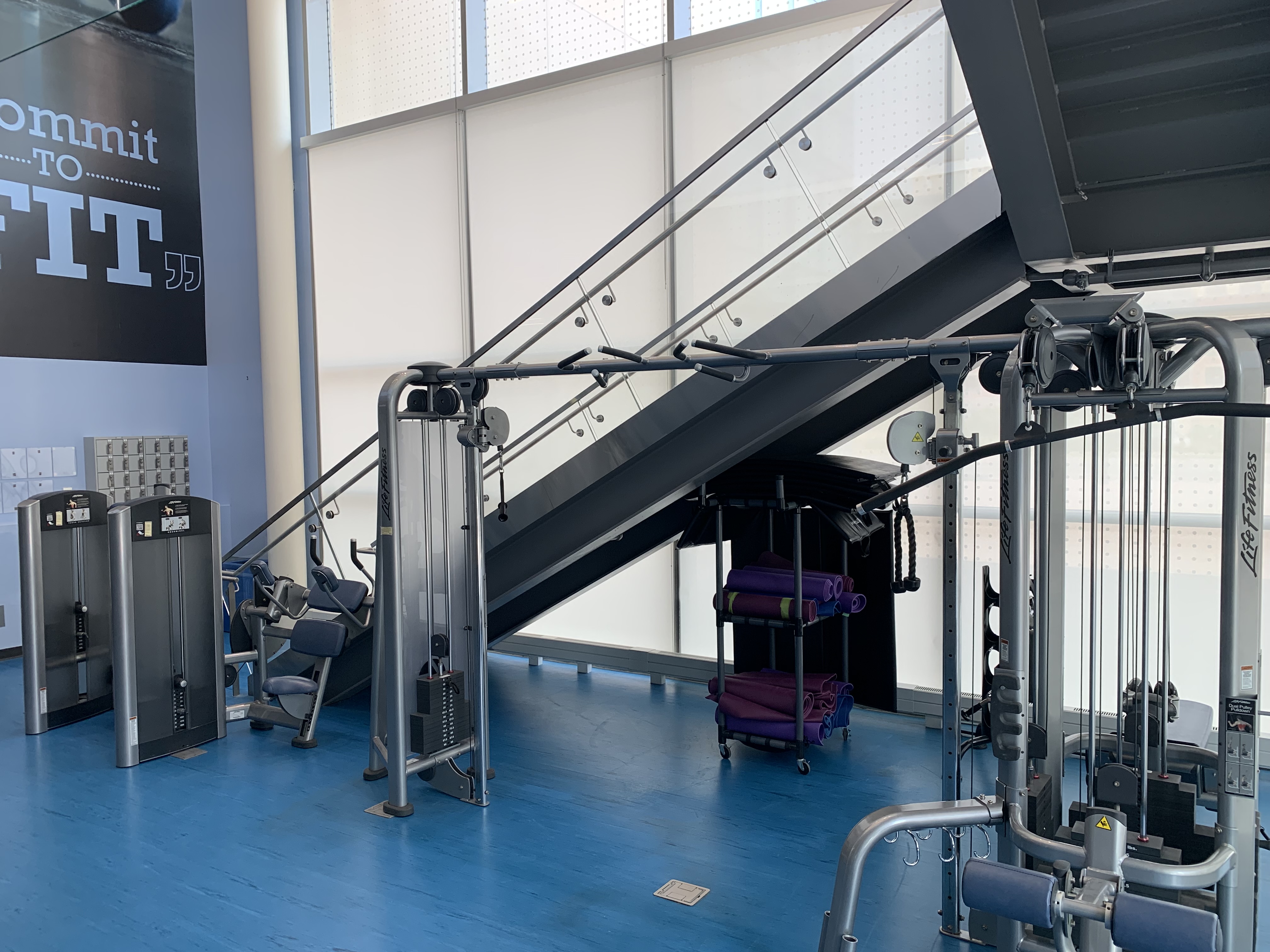 Gym interior with machines and a staircase to a 2nd floor.