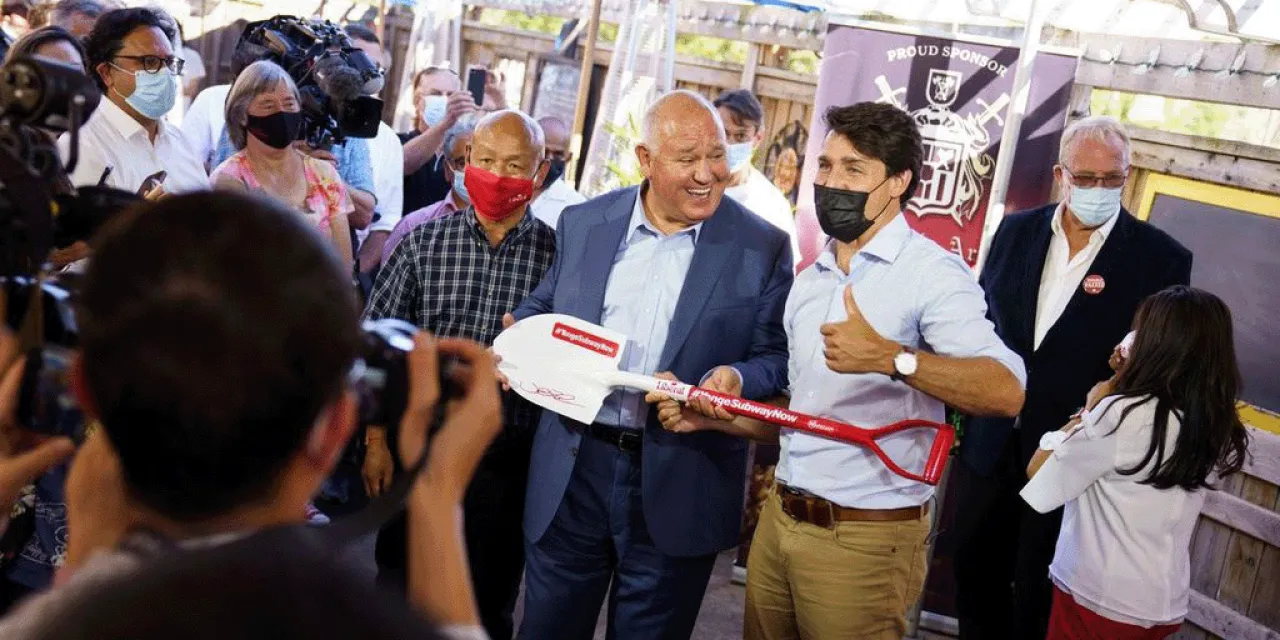 Justin Trudeau and Frank Scrapitti holding a shovel while being photographed by press.