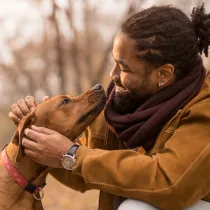 Person in outdoors smiling while petting a dog.