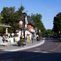 Sidewalk of people walking adjacent to a road with cars on it.