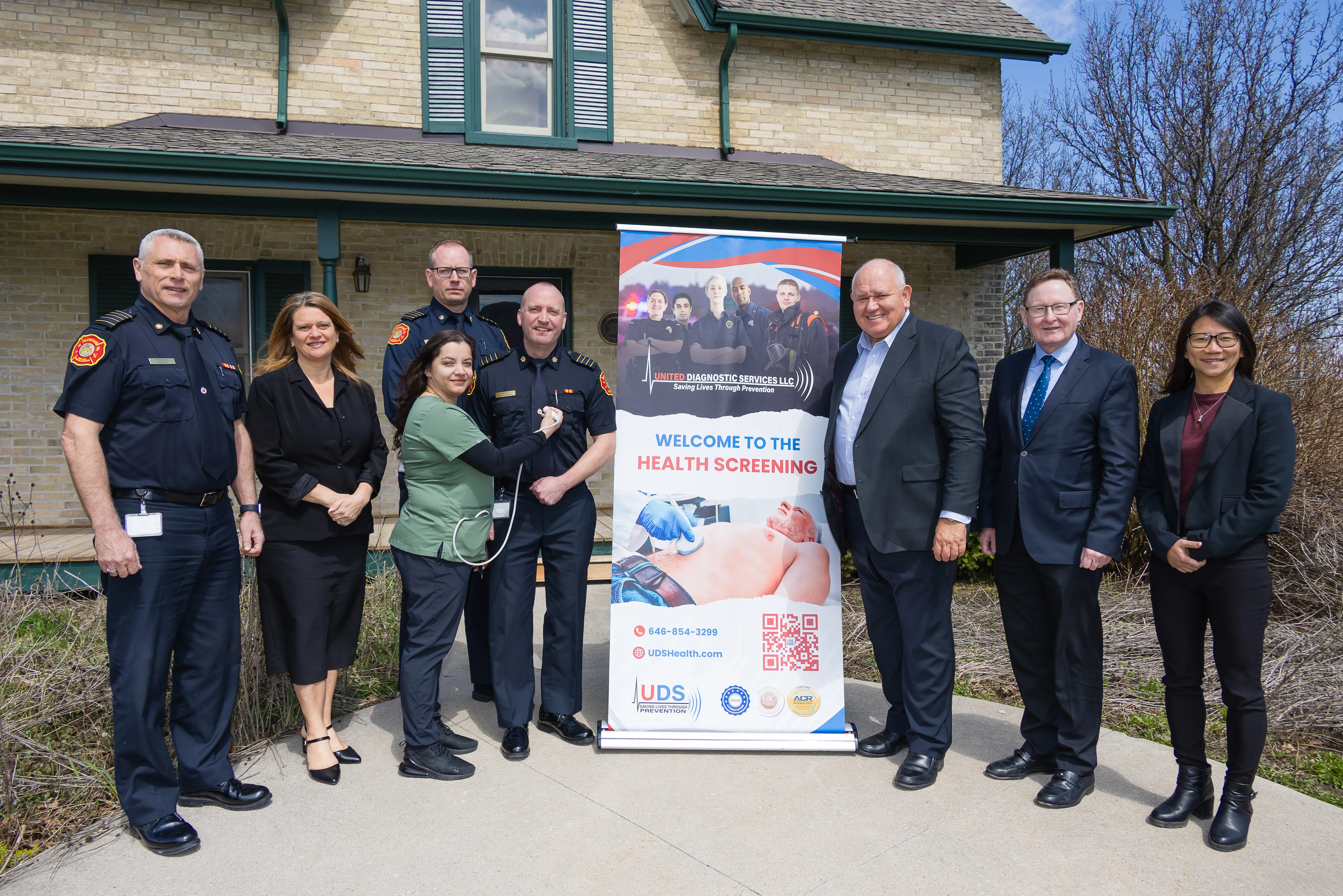 City staff and fire chiefs standing beside a "Welcome to the Health Screening" sign.