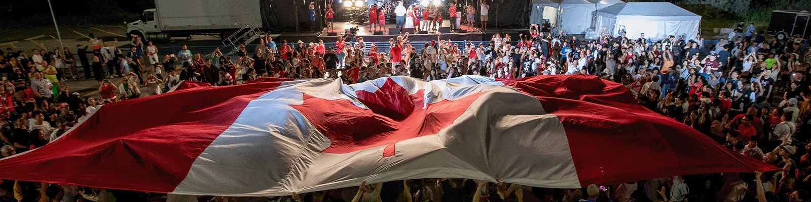 Crowd holding large Canadian flag.
