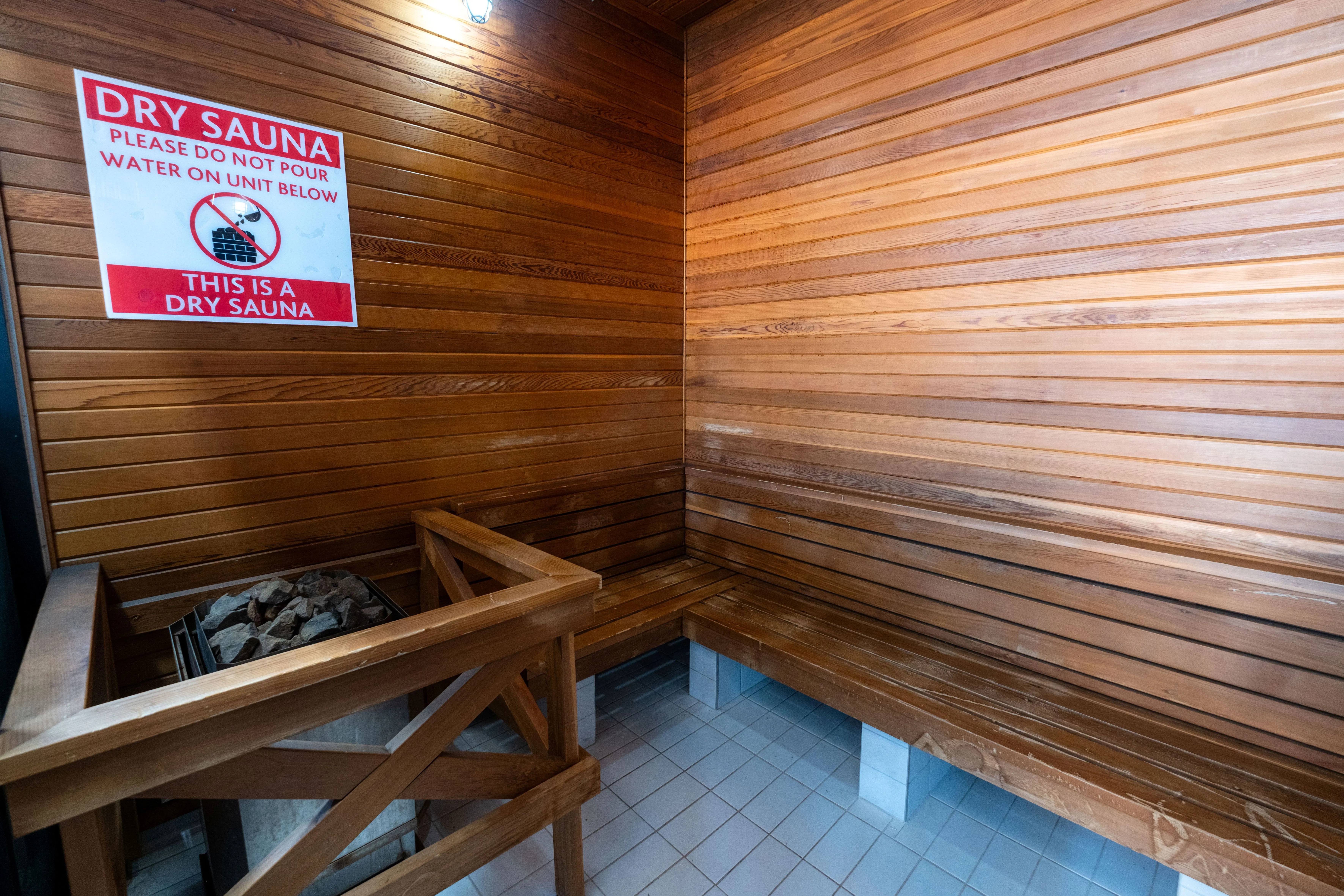 Interior of a wooden dry sauna with a bench and a sign warning not to pour water on the heater stones.