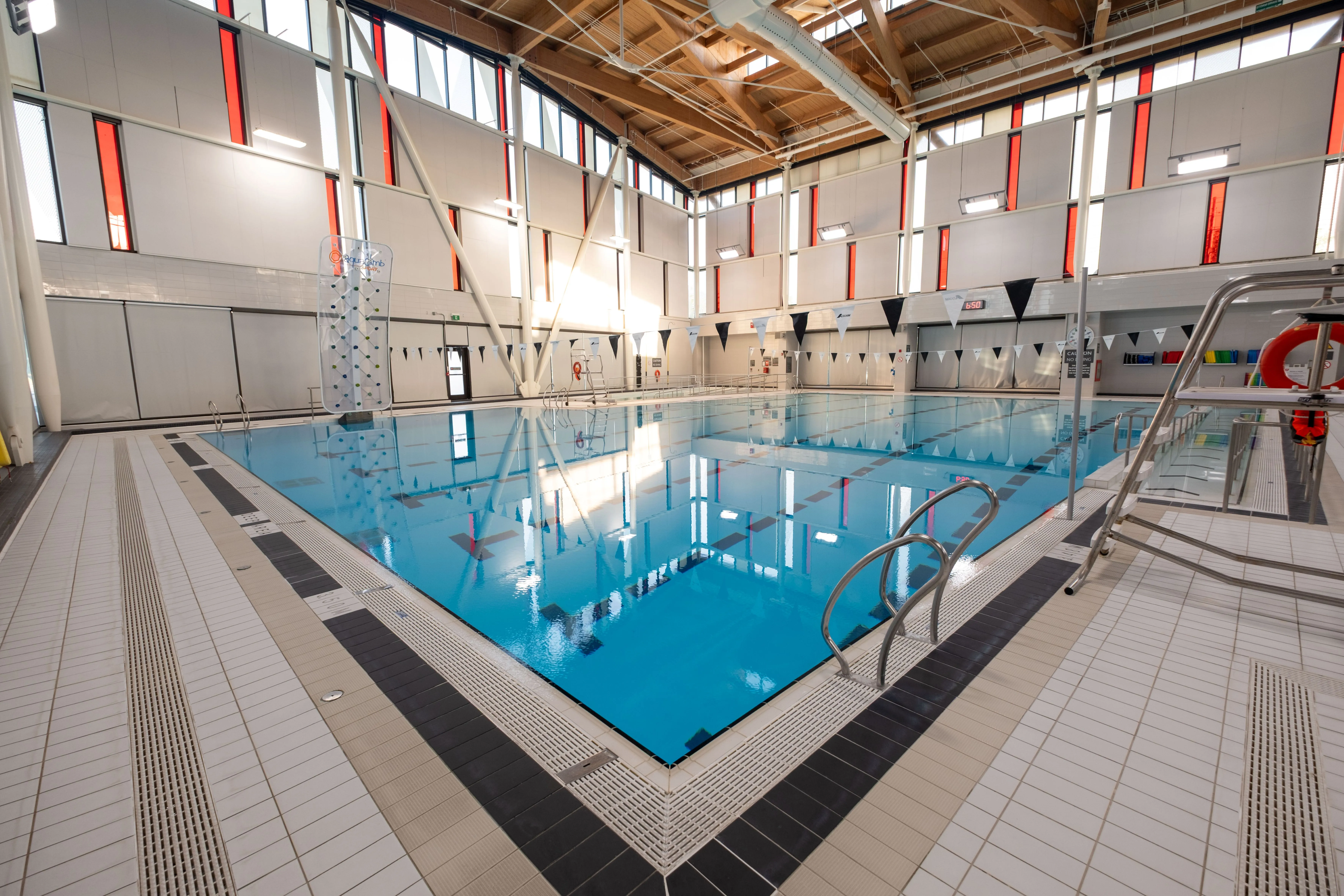 Indoor swimming pool with clear blue water, surrounded by tiled flooring and windows letting in natural light.