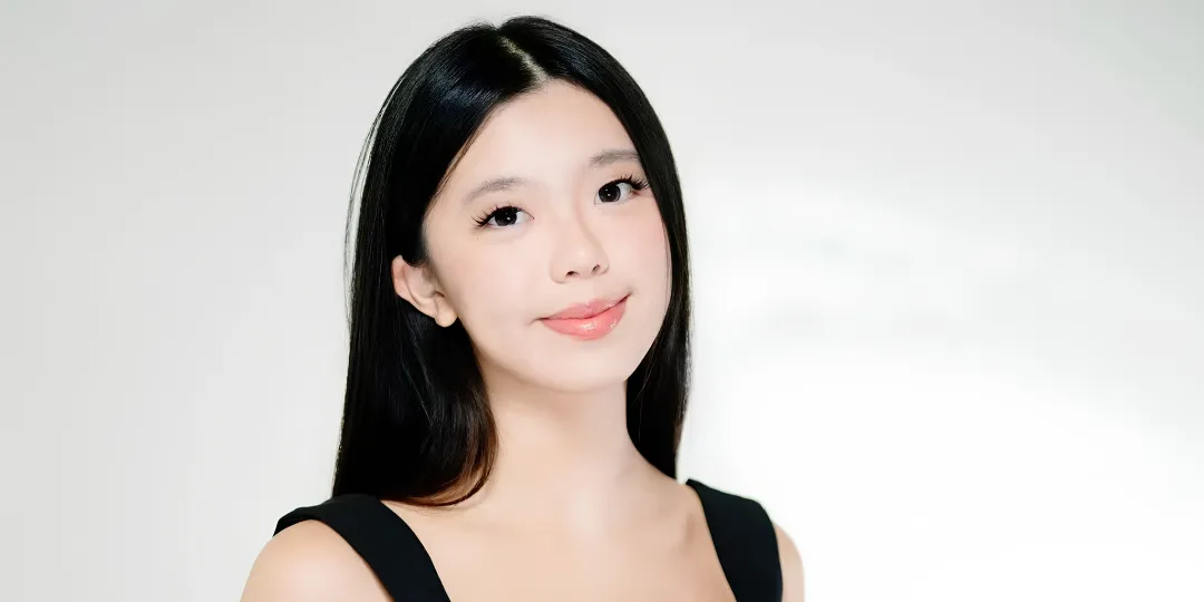 Portrait of performer Melinda Song with long dark hair wearing a black sleeveless top, facing the camera against a light gray background